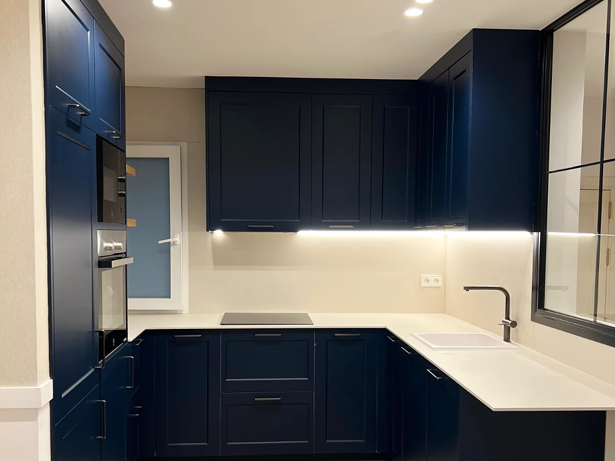 Cocina en U con frentes azul marino, encimera clara e iluminación bajo los muebles altos.